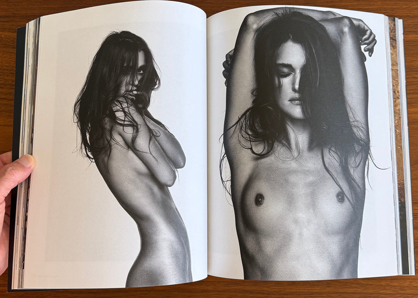 Open book showing black and white images of a nude woman on a wooden surface.