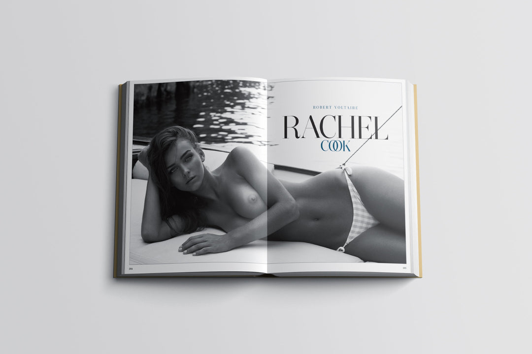 An open book or magazine laid flat on a light gray background, showing a grayscale cover spread with a reclining woman on the left page and the title 'RACHEL COOK' on the right page.